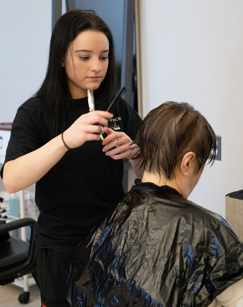 Een student knipt het haar van een vrouw.