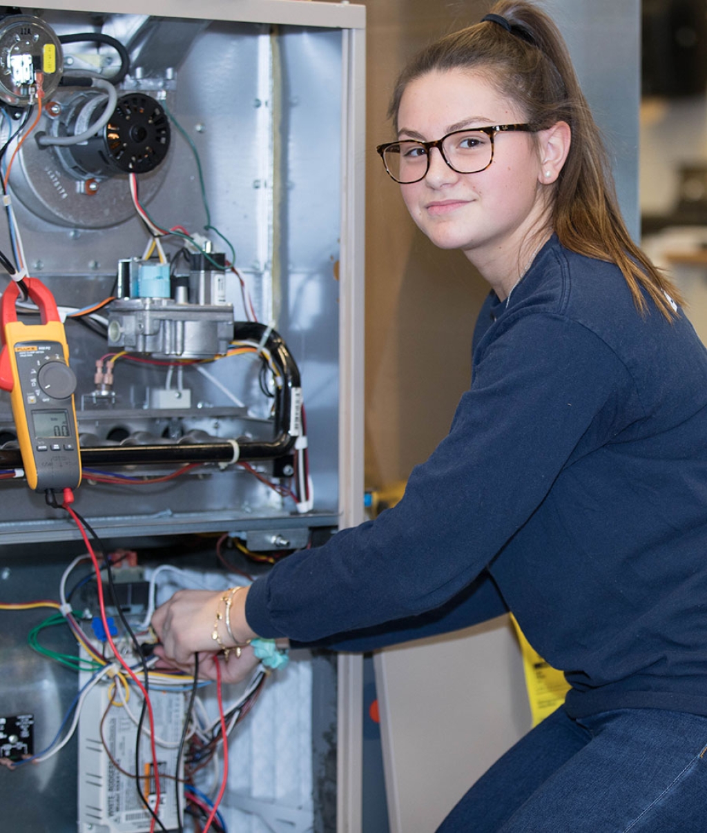 A female student works on an HVAC unit,