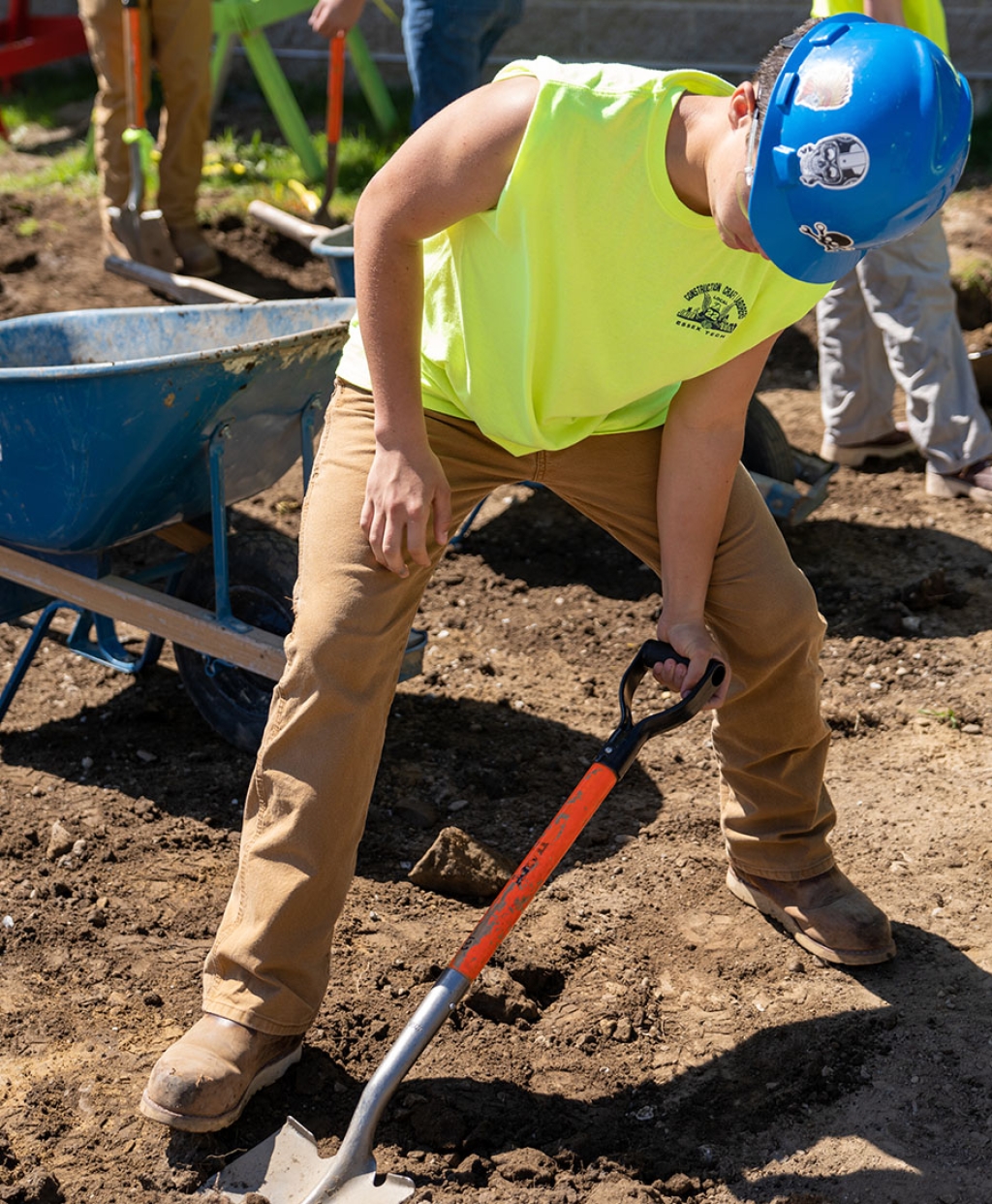 Un estudiante palea tierra en un sitio de construcción.