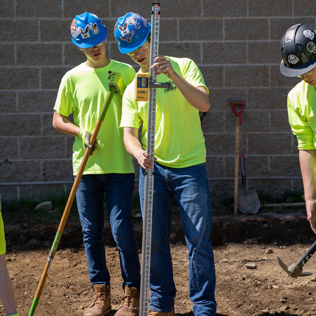 Students use measuring equipment at a construction site.