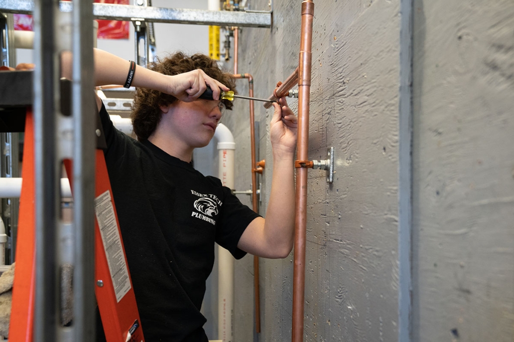Um aluno aparafusa um acoplamento em um tubo de cobre.