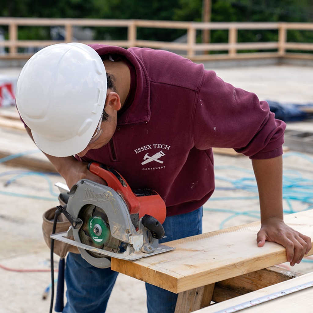 Un estudiante usa una sierra circular para cortar madera en un sitio de construcción.