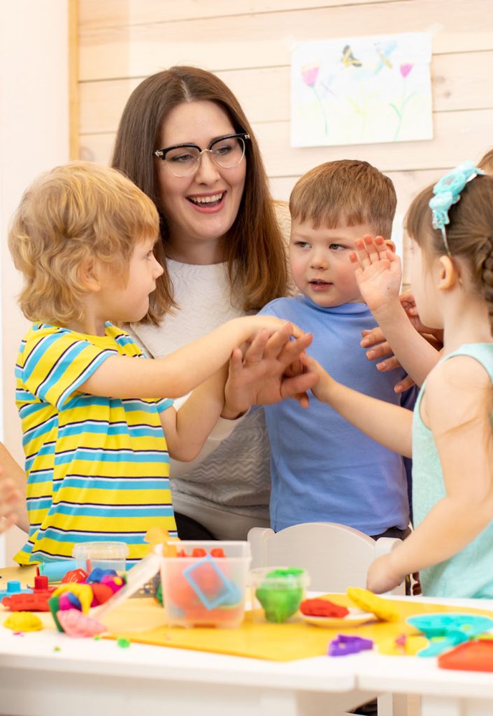 Una mujer joven interactúa con niños en edad preescolar.