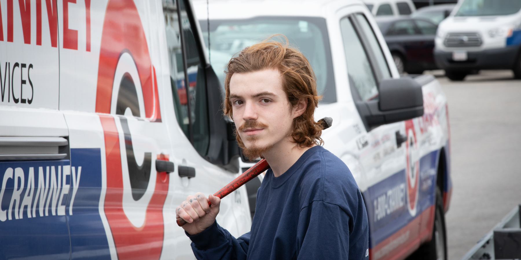 Estudiante de Educación Cooperativa frente a su camión de trabajo sosteniendo una llave para tubos.
