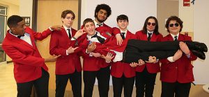 A row of SkillsUSA students in red jackets face the camera, they are holding up one of their members horizontally.