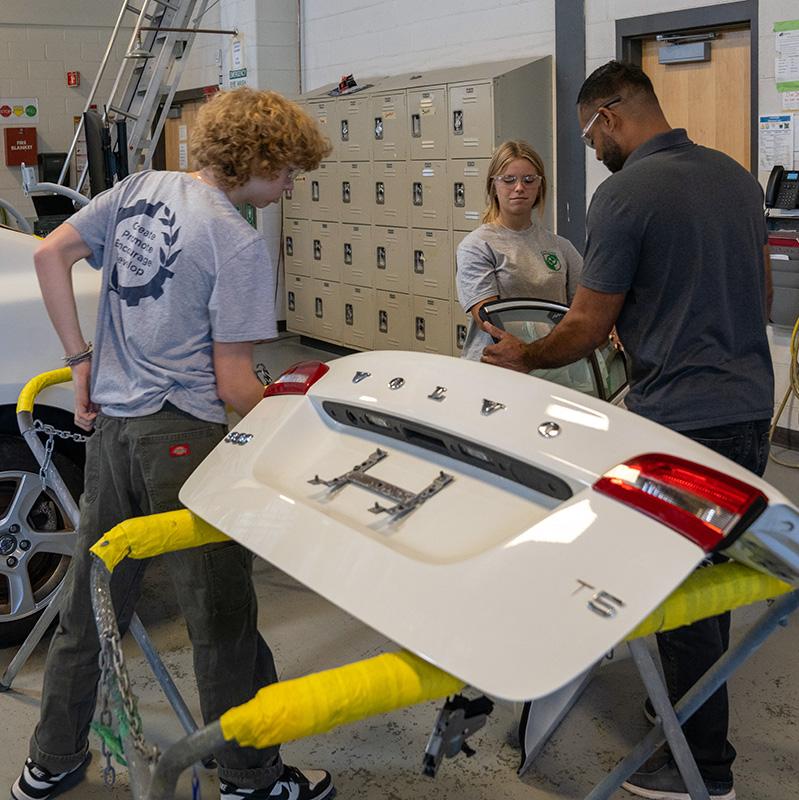 Two students and an instructor work on a car.